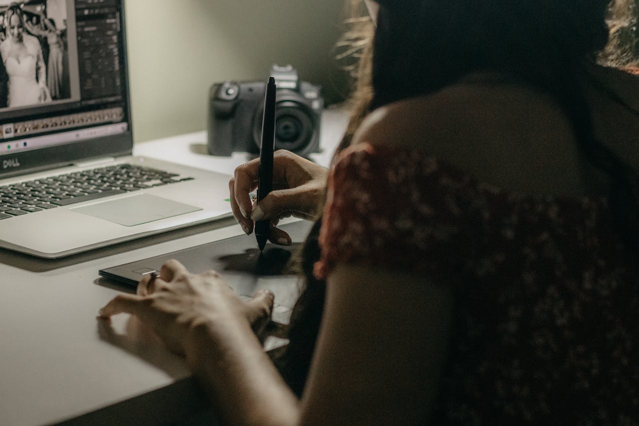 A woman uses a graphic tablet and laptop for photo editing in a modern workspace.